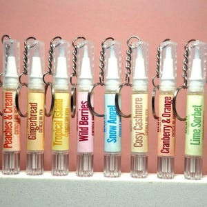 Puede incluir: Una fila de ocho bolígrafos de aceite para cutículas de plástico transparente con llaveros plateados. Cada bolígrafo tiene una etiqueta con un nombre de aroma único: Peaches & Cream, Gingerbread, Tropical Island, Wild Berries, Snow Angel, Cosy Cashmere, Cranberry & Orange y Lime Sorbet.
