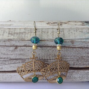 May include: A pair of gold filigree earrings featuring teal blue and green glass beads. The earrings have a delicate, intricate design and are perfect for adding a touch of elegance to any outfit.