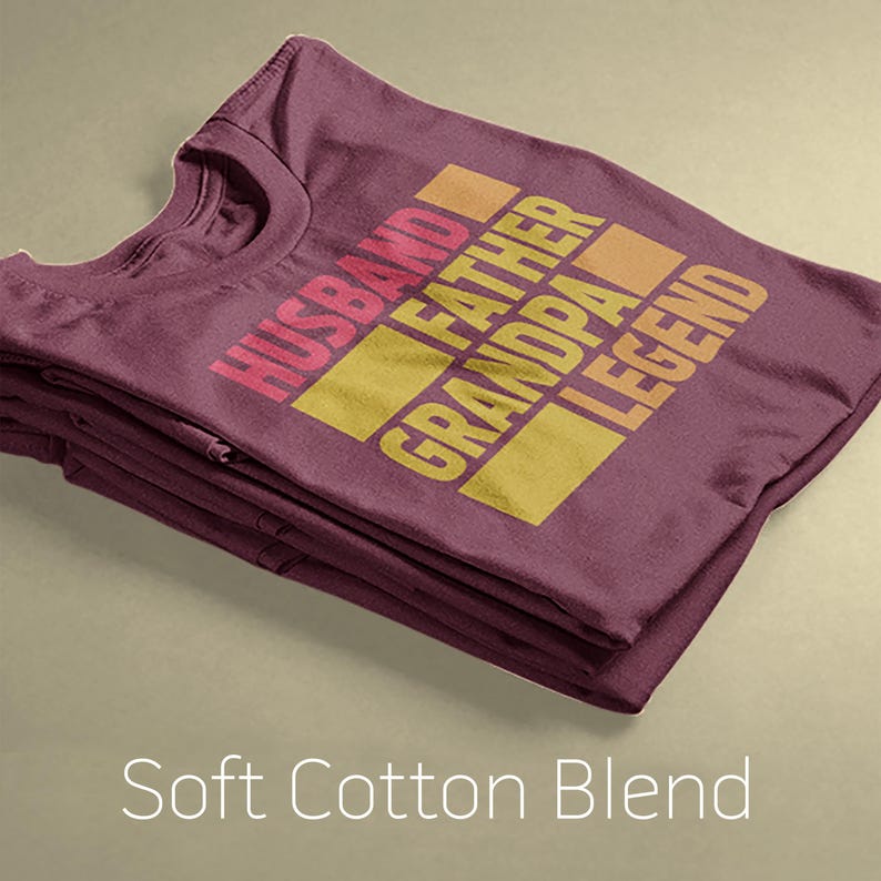May include: Folded maroon t-shirt with the words "HUSBAND FATHER GRANDPA LEGEND" in a gradient of pink, orange, and yellow. The words are stacked in a rectangular design. The text "Soft Cotton Blend" is at the bottom.