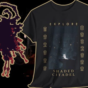 May include: Black t-shirt with a graphic featuring a white creature on a cliff under a starry sky. The text "EXPLORE" and "SHADED CITADEL" are printed on the shirt, along with stylized characters. The shirt has a gold-colored trim.