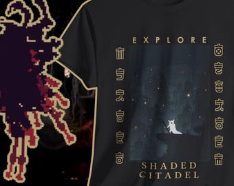 May include: Black t-shirt with a graphic featuring a white creature on a cliff under a starry sky. The text "EXPLORE" and "SHADED CITADEL" are printed on the shirt, along with stylized characters. The shirt has a gold-colored trim.