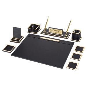 Peut inclure: Un ensemble d'accessoires de bureau noir et doré comprenant un grand sous-main, une plaque nominative avec le texte Arif YOLCU Lawyer & Avukat, deux stylos dorés, un porte-stylo, un porte-cartes, un porte-notes et quatre sous-verres carrés.