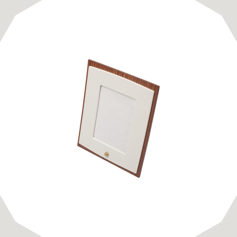 Op de afbeelding: Een rechthoekige fotolijst met een donkerbruine houtnerfrand en een gladde witte passe-partout. De lijst is verticaal geori&euml;nteerd en bevat een kleine, ronde, goudkleurige metalen knop in het midden aan de onderkant van de witte mat.