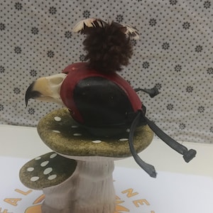 May include: A small, hand-crafted bird figurine with a red, black, and white painted design. The bird is perched on a green and white mushroom-shaped base.