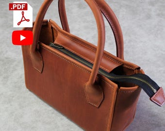 May include: A brown leather tote bag with a top zipper closure and two handles. The bag is open and the zipper is pulled down.