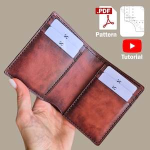 Puede incluir: Cartera de cuero marrón abierta con ranuras para tarjetas, que contiene tarjetas blancas con el logotipo "S". La cartera se sostiene abierta, mostrando su interior. Iconos para un patrón PDF y un tutorial de YouTube.