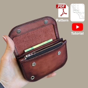 Puede incluir: Cartera de cuero marrón abierta con un compartimento con cremallera y cierres de botón a presión. La cartera contiene una pequeña cantidad de efectivo. La imagen también incluye iconos para un patrón PDF y un tutorial.