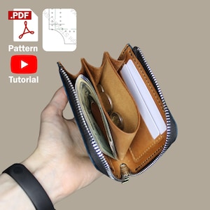 Könnte beinhalten: Ein kleines, offenes Lederportemonnaie mit Reißverschluss, das Bargeld, Münzen und Karten enthält. Das Portemonnaie ist braun und schwarz, mit einem hellbraunen Innenraum. Das Bild enthält auch ein PDF-Muster und ein YouTube-Tutorial-Symbol.