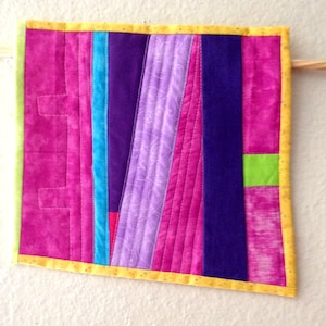 May include: A colorful patchwork quilt with a yellow border. The quilt is made up of various shades of pink, purple, blue, and green fabric.