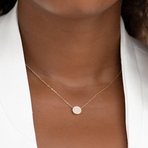 May include: A delicate gold chain necklace with a small, round pendant encrusted with tiny white stones.