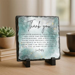 May include: A square slate plaque with a teal and gold watercolor design and the words "Thank you" in elegant script. The plaque includes a heartfelt message of gratitude and sits on a black stand. A succulent and a coffee cup are in the background.