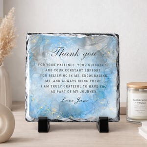 May include: A square slate plaque with a blue and white watercolor design. The text "Thank you" is at the top, followed by a message of gratitude and the name "Love Jane". The plaque is displayed on a black stand.