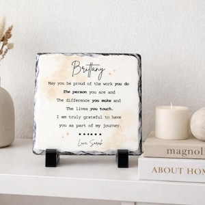 May include: A square slate plaque with a personalized message for "Brittany." The text is in black script and includes a message of appreciation. The plaque is propped up on a black stand, with a candle and books in the background.