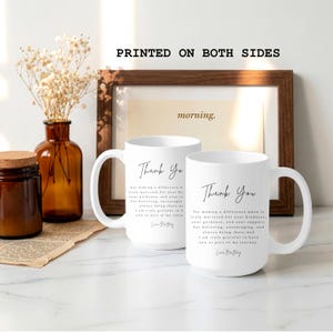 Puede incluir: Dos tazas de cer&aacute;mica blancas con las palabras "Thank You" en elegante escritura negra. Las tazas tienen un asa curva y un mensaje impreso en ambos lados. El fondo incluye una impresi&oacute;n enmarcada y objetos decorativos.