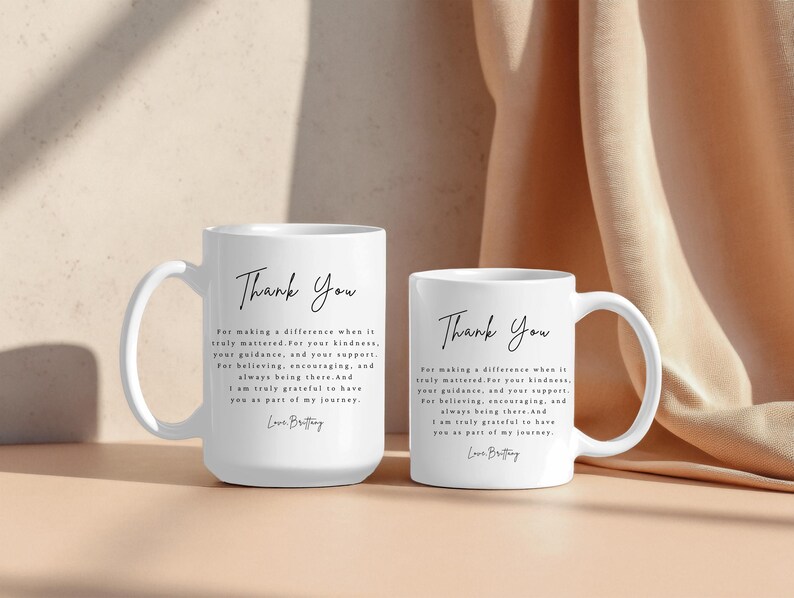 Puede incluir: Dos tazas de cer&aacute;mica blancas con las palabras "Thank You" en escritura elegante. Las tazas tienen un asa curva y un mensaje impreso debajo del texto. El fondo es beige neutro.