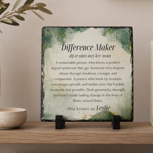 May include: A square slate plaque with rough, chiseled edges featuring a green and white watercolor-style background with gold accents. The text reads: Difference Maker, dif-er-uhns mey-ker, noun, followed by a definition and Also known as: Leslie.