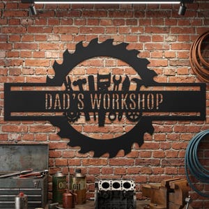 May include: Black metal sign reading "DAD'S WORKSHOP" with a circular saw blade design. The sign features silhouettes of tools and gears, mounted on a brick wall. The workshop theme is evident.