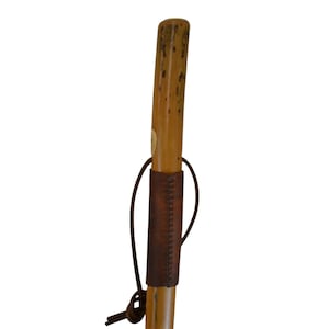 May include: A wooden walking stick with a natural finish. It features a brown leather grip stitched with a darker thread. A leather loop is attached near the bottom.
