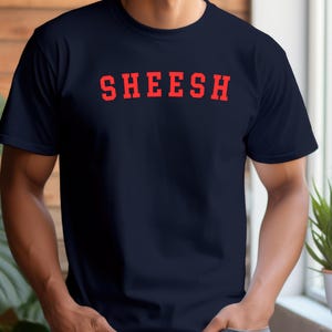 May include: A navy blue t-shirt with the word "SHEESH" printed in red letters.