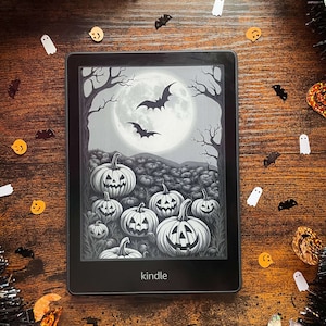 May include: A black and white illustration of a field of jack-o'-lanterns under a full moon with bats flying overhead, displayed on a Kindle e-reader.