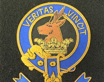 Puede incluir: Un escudo bordado azul y dorado con una cabeza de ciervo, una corona y el texto "VERITAS VINCIT" y "KEITH".