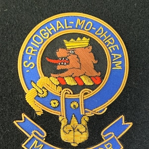 Peut inclure: Un blason brodé en bleu et or avec un lion et le texte "S-RIOGHAL-MO-DHREAM MACGREGOR".