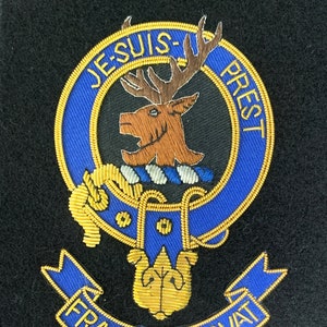 May include: A blue and gold embroidered crest with a stag's head, a knot of rope, and a banner reading "Fraser of Lovat". The crest is surrounded by a blue circle with the text "Je Suis Prest" in gold.