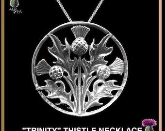 Puede incluir: Un collar con un colgante de plata que presenta un diseño circular con tres cardos estilizados. El colgante está en una cadena de plata y el texto "TRINITY" THISTLE NECKLACE está debajo del colgante.
