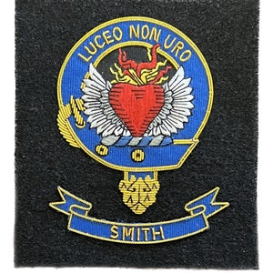 May include: A blue and gold embroidered crest with a heart, wings, and the text "LUCEO NON URO" above a banner with the text "SMITH".