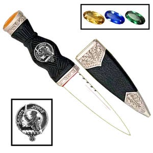 May include: A black and silver Scottish Sgian Dubh with a silver lion crest and a black leather scabbard. The handle is decorated with a black and white checkered pattern.
