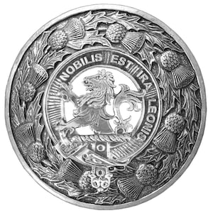 May include: A silver metal Scottish clan crest featuring a lion rampant with a crown and the text "Nobilis Est Ira Leonis" surrounded by a wreath of thistles.