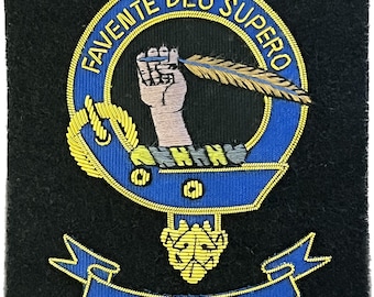 Op de afbeelding: Een blauw en gouden geborduurd wapenschild met de tekst "FAVENTE DEO SUPERO" en "MITCHELL" op een zwarte achtergrond.