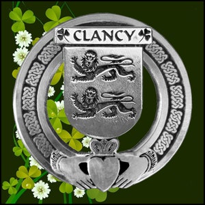 May include: A silver Celtic knot design with a silver shield featuring two lions and the text "CLANCY" above the shield. The shield is surrounded by a silver Celtic knot design. A silver Claddagh ring is below the shield.