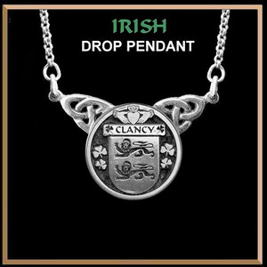 May include: Silver Irish drop pendant necklace with a Celtic knot design and a round charm featuring the Clancy family crest with three lions and shamrocks. The charm also includes the text "Clancy" in a banner.