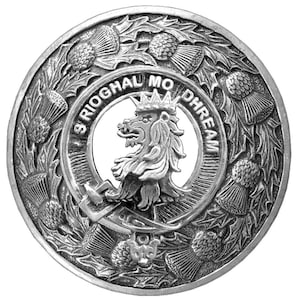 May include: A silver-toned metal clan crest with a lion's head and the text "S'RIOGHAL MO DHREAM" surrounded by a wreath of thistle flowers.