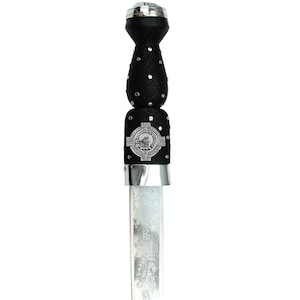 May include: A Scottish dirk featuring a black handle with silver detailing. The handle has a woven texture and is studded with silver. A silver emblem is set on the handle. The blade is etched with a floral pattern.