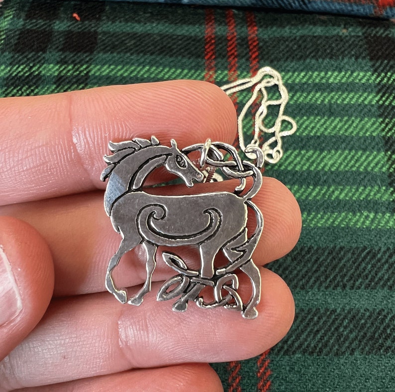 May include: A silver Celtic knot pendant necklace featuring a stylized horse design. The pendant is detailed with intricate knotwork and a swirling pattern.