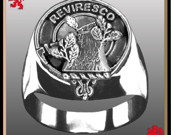 Puede incluir: Un anillo de plata con un escudo negro y blanco que presenta un tocón de árbol con hojas y el texto "REVIRESCO".