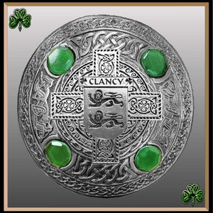 May include: A silver Celtic knotwork kilt pin with green gemstones and the name "Clancy" inscribed on a shield.