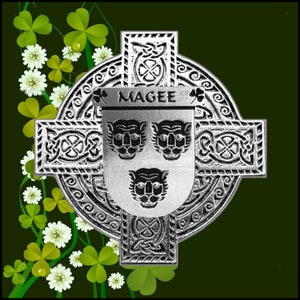 May include: A detailed silver Celtic cross design featuring knotwork and a central shield. The shield displays three tiger faces and the name "MAGEE". The background is dark green with shamrocks and white flowers.