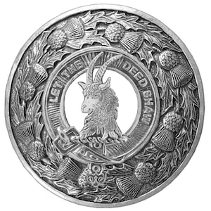 May include: A silver circular emblem featuring a goat within a ring inscribed with "LET THE DEED SHAW". The design is surrounded by thistle and leaf motifs, creating a detailed, decorative border.