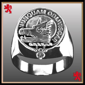May include: A silver ring with a round crest featuring a wolf's head and the text "NUNQUAM OBLIVISCI".