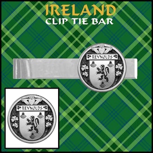 Könnte beinhalten: Eine silberfarbene Krawattenklammer mit den Worten "Ireland" und "Clip Tie Bar" in goldfarbenen Buchstaben. Sie zeigt ein rundes Emblem mit dem Namen "Reynolds", einem Löwen und Kleeblättern. Der Hintergrund ist ein grün-blaues Karomuster.