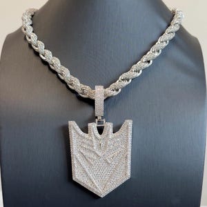 May include: A silver-toned rope chain necklace featuring a large, shield-shaped pendant. Both the thick, twisted chain and the flat, geometric pendant are covered in small, clear, sparkling stones that create a uniform, reflective, and metallic appearance.