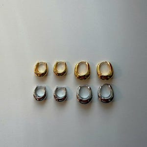 May include: Eight oval-shaped hoop earrings in two sets of four. The top row features gold-toned earrings, while the bottom row displays silver-toned earrings. The earrings are displayed on a white surface.