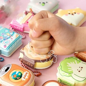 May include: A collection of colorful, cartoon-themed, squishy keychains. The keychains feature various food and drink items, such as a donut, a can of juice, and a head of lettuce. The keychains are made of soft, squeezable material and are perfect for adding a touch of fun to your keys or bag.