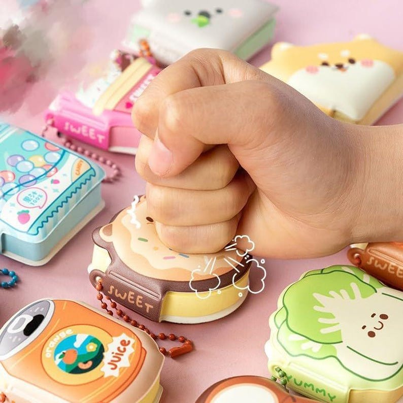 May include: A collection of colorful, cartoon-themed, squishy keychains. The keychains feature various food and drink items, such as a donut, a can of juice, and a head of lettuce. The keychains are made of soft, squeezable material and are perfect for adding a touch of fun to your keys or bag.