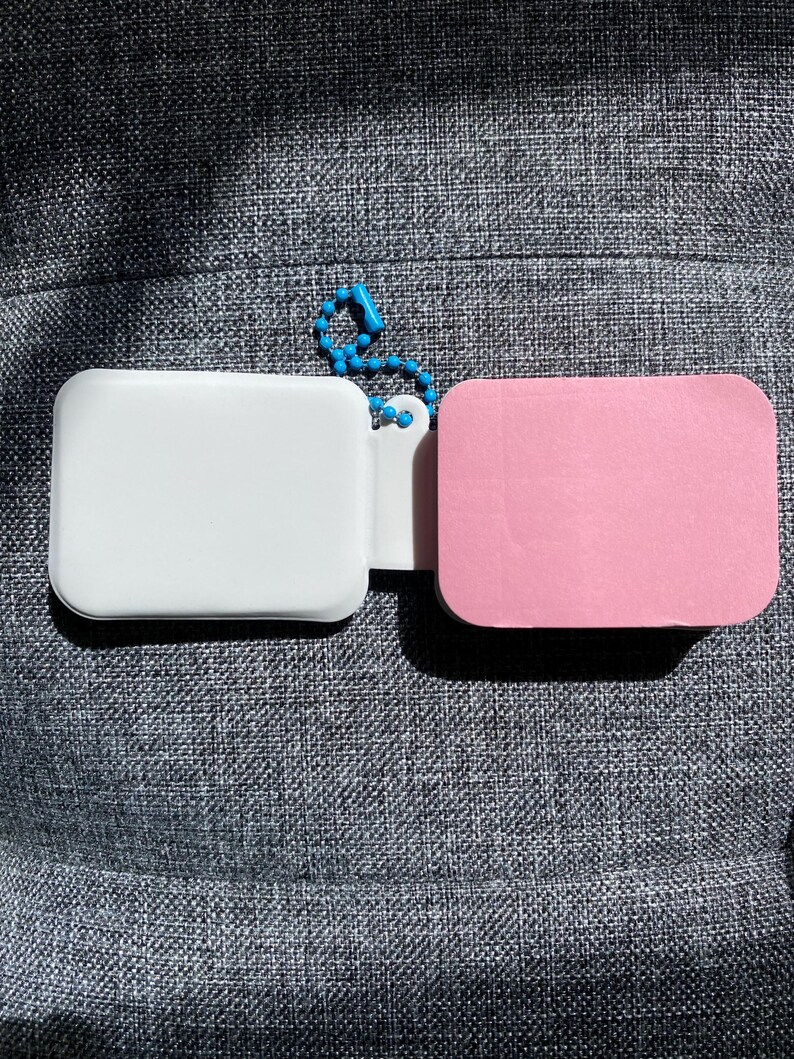 May include: Two small rectangular keychains, one white and one pink, connected by a blue beaded chain.