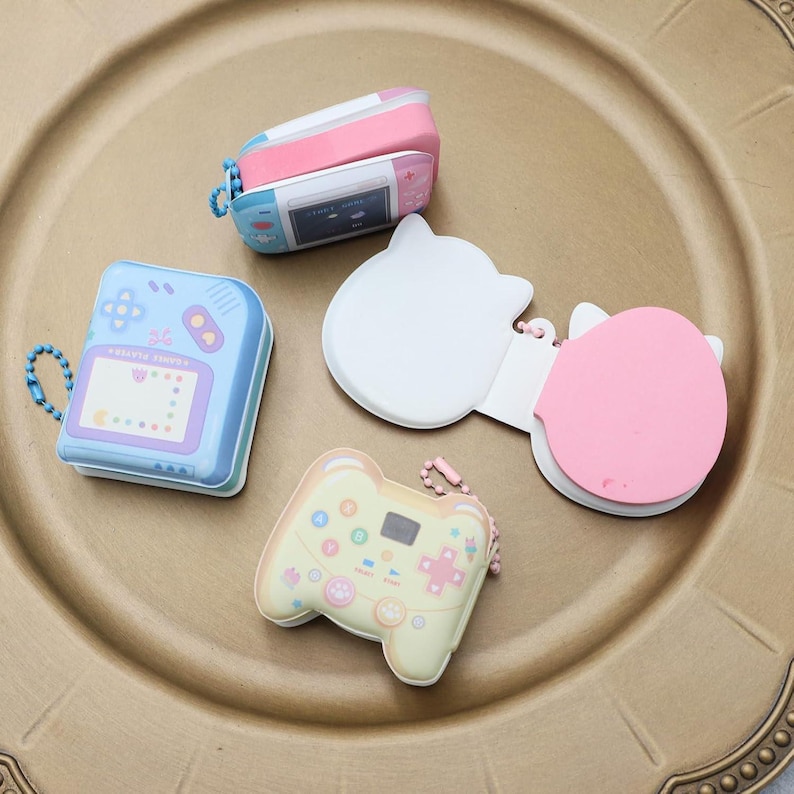 May include: Four colorful mini notepad sets shaped like video game controllers and handheld game consoles. Each notepad has a keychain attached.