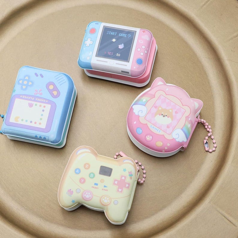 May include: Four colorful keychain charms shaped like handheld video game consoles. The charms are pink, blue, yellow, and white with cartoon graphics and text. The text on the charms reads "START GAME", "GALAXY STAR", "GAME", and "START".